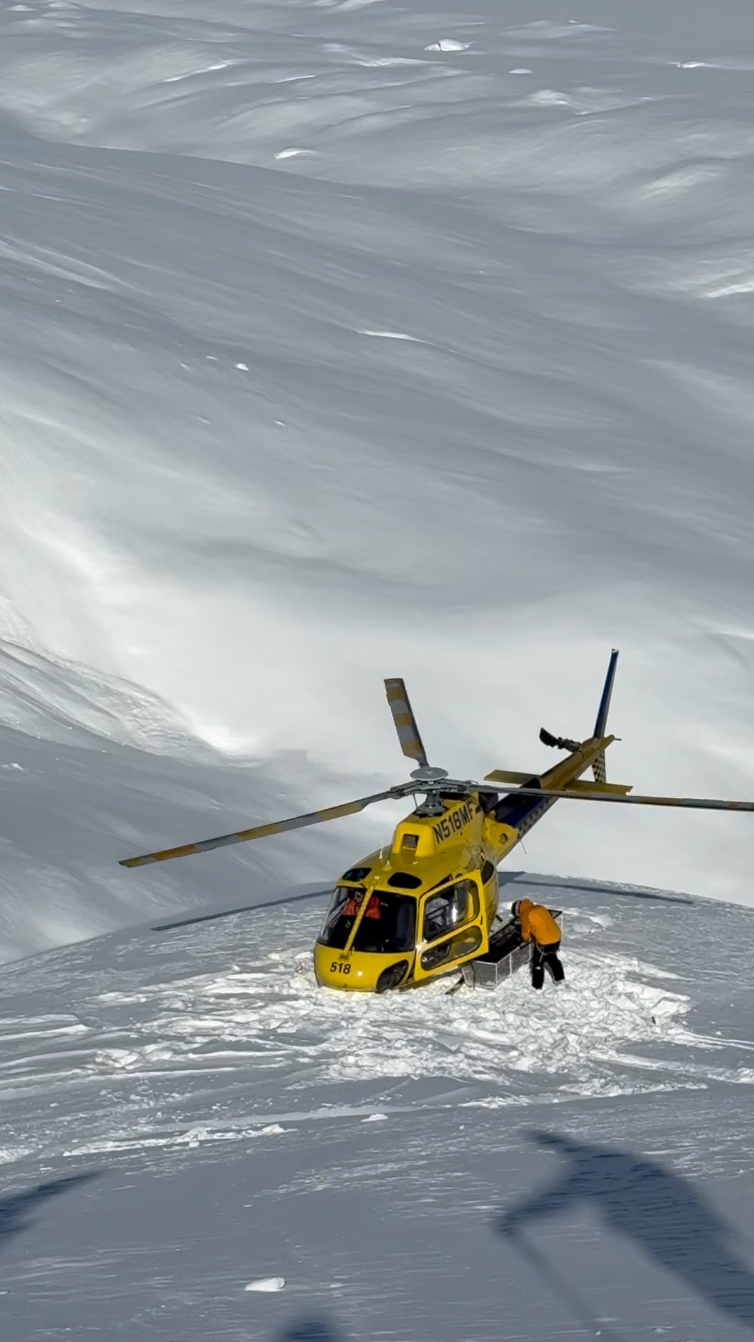 Yellow helicopter and a person on a mountain snowfield
