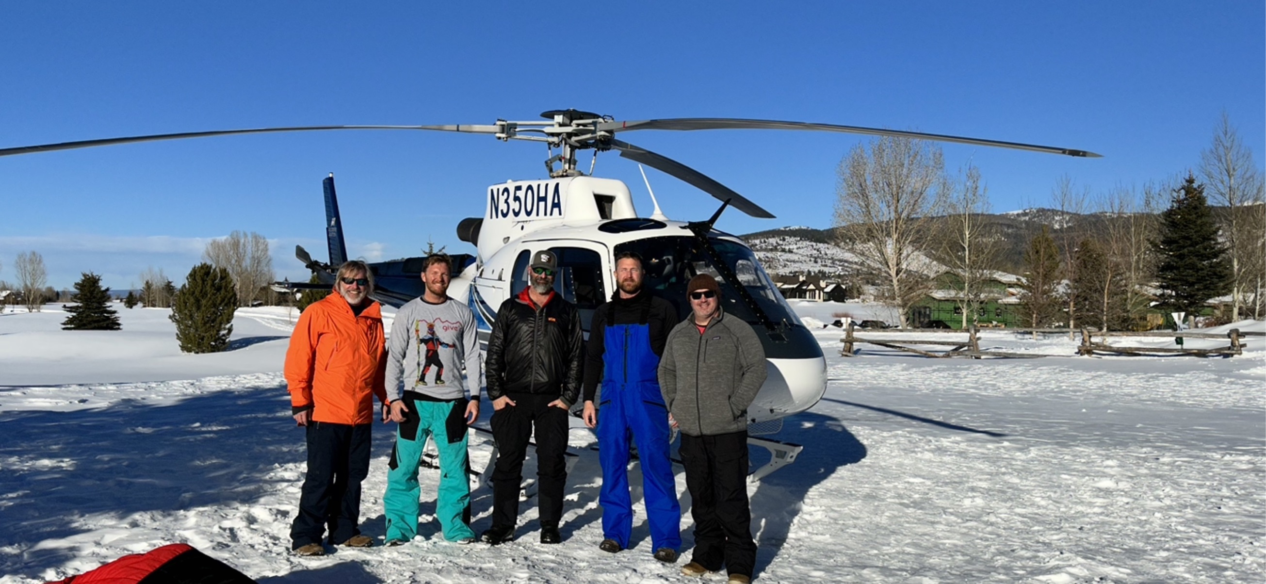 Five people standing together in front of a helicopter